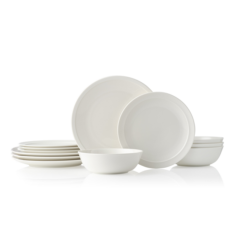 A collection of Adam Liaw Everyday Noritake dinnerware, including white porcelain plates and bowls, some stacked and some arranged with food.
