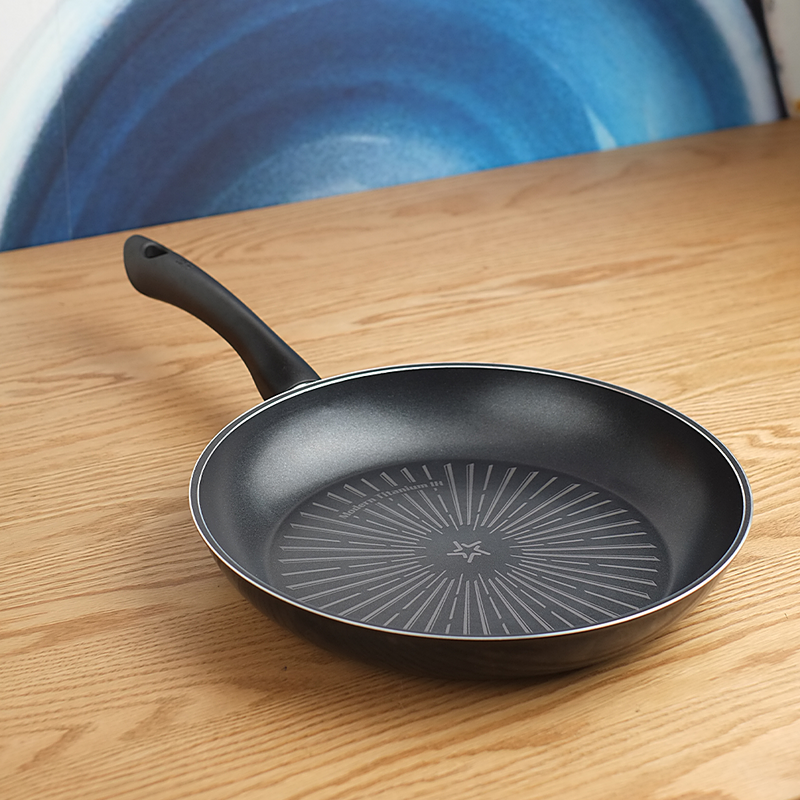 The black 28cm Happycall Modern Titanium Nonstick Induction Frypan, resting on a light wood tabletop with a blue abstract background.
