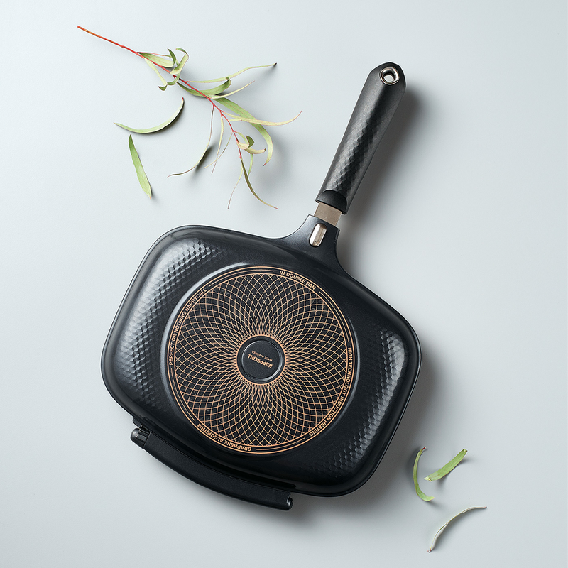 The closed Happycall IH Synchro Double Pan, angled to show the circular induction base on its textured grey exterior.