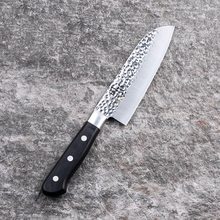 Kai Seki Magoroku Hammered Santoku Knife 145mm, showcasing its elegant hammered blade finish and ergonomic black handle against a stone surface.