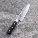 Kai Seki Magoroku Hammered Santoku Knife 145mm, showcasing its elegant hammered blade finish and ergonomic black handle against a stone surface.