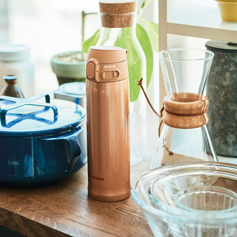 A studio photo of the Zojirushi SM-TA48 TUFF vacuum insulated flask in gold, shown from the front highlighting its one-touch release lid and locking switch.