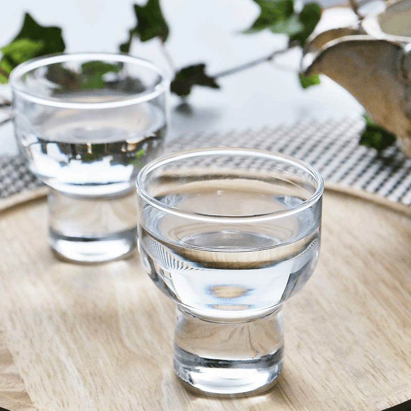 A styled lifestyle photo of two Toyo Sasaki sake glasses filled with clear liquid, presented on a wooden tray to show a serving suggestion.