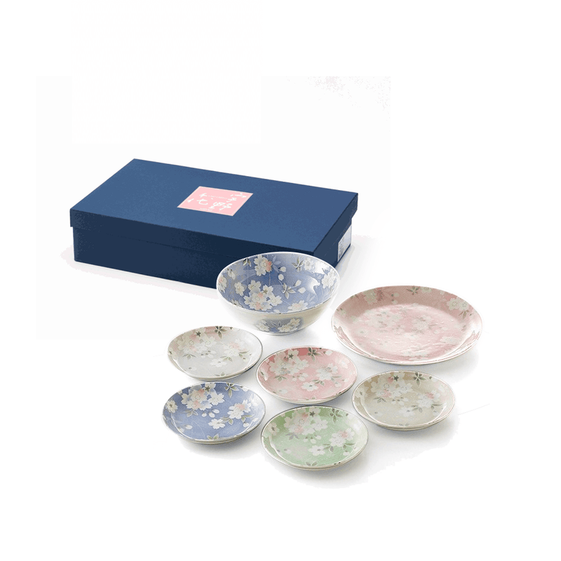 The Aito Mino Yaki Uno Chiyo Blossom 7-piece dinnerware set, including a large bowl, large plate, and five small plates in assorted colours with cherry blossom designs, displayed next to its blue gift box.