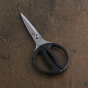 The Kai Seki Magoroku kitchen scissors with black ergonomic handles, shown resting on a dark wood table.
