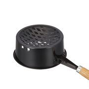 A close-up, angled view of the Nagatsuka charcoal starter pan, highlighting the black enamel finish and the perforated grid at the bottom for airflow.
