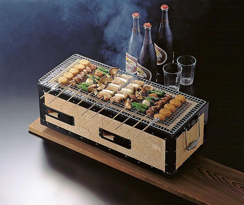 kunoto Japanese Konro Grill - Medium 54cm in action with skewers of meat and vegetables grilling on top, accompanied by two bottles of beverages and glasses on a wooden platform.