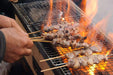Close-up of skewered meats being grilled on an Okunoto Japanese Konro Grill with flames rising.