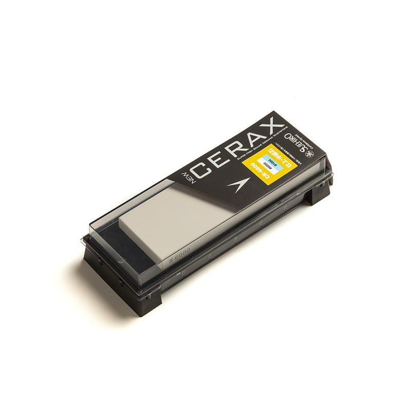 The Suehiro NEW CERAX CR-4800 two-sided whetstone shown inside its combination storage case and sharpening base, with a transparent lid.
